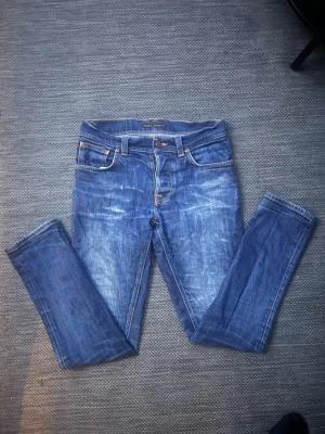 Nudie Jeans blå jeans W30 L32 - Säljer ett par klassiska blå jeans från Nudie Jeans. De har perfekt passform och mkt sköna. Detta är ett ryktigt schysst par, med riktigt fet tvätt och slitningar. De är i storlek 30/32 (W30 & L32). De passar väldigt bra till nästan allt, vilket gör dem väldigt lätt att matcha. Jag skulle säga att 329kr är ett väldigt bra pris för ett par i detta skick och utseende! Nypris: 1800 typ & skick: 9,5/10 (nästan nya). Hör bara av dig vid minsta fundering och priset är inte hugget i sten! Mvh Erik!