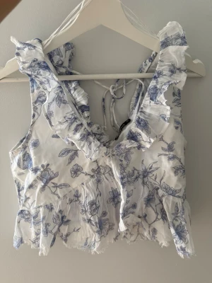 Topp GinaTricot  - En söt peplumtopp från GinaTricot med blåvitt blommönster, avklippt design nedtill (ska vara så dvs och inget jag klippt av).  Storlek; XS Skick; Ny dock borttagna lappar Material; 100% bomull  #ginatricot #sommartopp #blommig #peplum #scandi #sommar