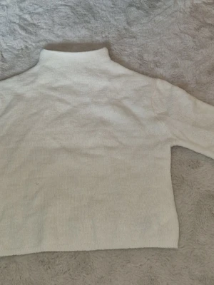 Beige stickad tröja med halvpolokrage - Mysig beige stickad tröja med halvpolokrage och trekvartsärmar. Tröjan har en rak passform och är tillverkad i ett mjukt material som känns skönt mot huden. Perfekt för lager på lager och enkel att matcha med olika outfits. Om man är känslig så kan den upplevas att klia lite men det är lugnt om man har en tröja under. Aldrig använd. Pris kan ändras.