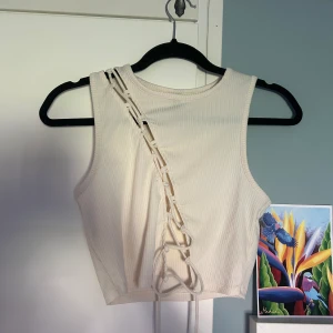 Croppat linne med snörning  - Färgen är vit men mer åt créme-hållet. Använd endast en gång och är i bra skick. Tyget är ribbat och stretchigt.