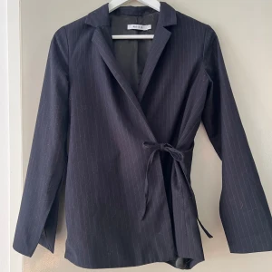 Kostymset från nakd i strl 34 och 36 - Kostymset från NAKD, marinblå med vita ränder. Högmidjade byxor. Kavaj med slits i armarna. Normal i storleken. Knappt använt. 34 i kavaj och 36 i byxor.