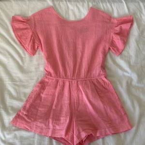 Jumpsuit  -  Rosa jams ut med shorts💗🌸 fina utsvängda ärmar med volanger🎀 snören som man knyter till rosett längst bak!