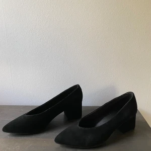 Oanvända pumps i mocka - Pumps Low heel i klassisk modell i mjuk mocka med bred, klädd klack och v-ringad fotöppning. Textilfodrad insida. Klackhöjd ca 5,5 cm i stl 37.  Endast provade. Nypris 499:- Små märken på sidan av båda skorna, syns inte jättetydligt  