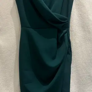 Vacker mörkgrön klänning av märket Katniss.  Figursydd med slits. Dragkedja i ryggen. Bekvämt material.   Strl: 36 men lite åt det mindre hållet. 