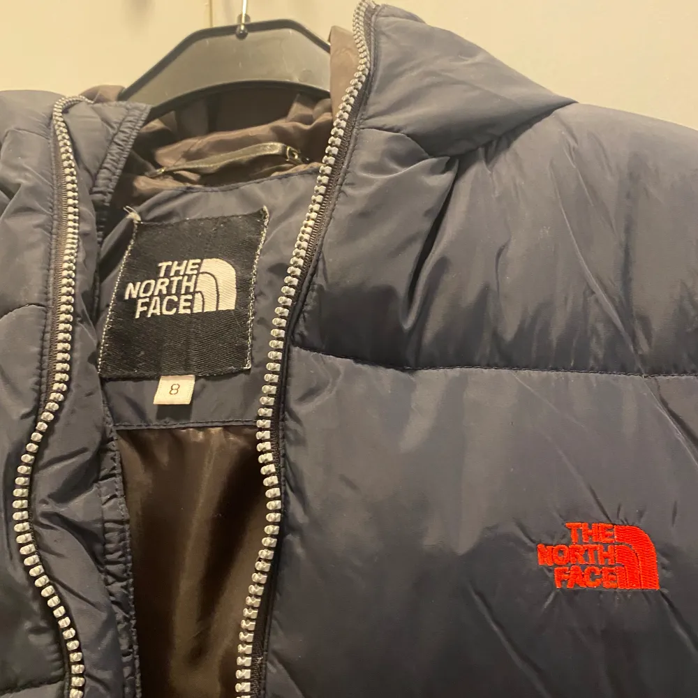 The North Face jacka för barn! I storlek 8 Som syns på de två sista bilderna är det skavanker. Det är lagat vid luvan men inget som syns eftersom luvan hänger ner och döljer det. Samt att det ej går spänna in nederkanten på ena sidan!  Frakt tillkomm. Jackor.