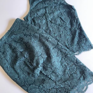 Topp Spets med kjol - Storlek 34 - Säljer en vacker, ärmlös spetsblus från H&M i storlek 34. Topppen är giord i genombruten spets med en läg stäkrage och har en elegant öppning bak med knytband i nacken. En knäläng kjol i spets med transparenta partier nedtill. Kjolen har dragkedja.