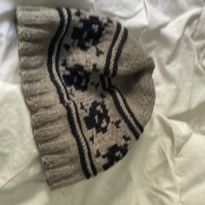 Stickad mössa med döskallar - Stickad mössa med döskallar, köpt på Plick men var för liten för mig att använda. Bra skick och inprincip oanvänd. I svart och grå färg, skulle säga passar för folk med mindre huvud.