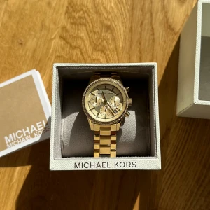 Michael Kors klocka - Guldig Michael Kors klocka i kartong,  nypris 2695kr.   Köpte den för ca 4 år sedan, har blivit lite ”nött” på vissa ställen som ni kan se på bild 3, därav billigt pris men de är inget man tänker på! Ej använt den på ca 3 år. 