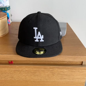 Svart LA keps - Hej säljer nu min svarta LA keps perfekt till sommaren och den nya stilen på tiktok(laidback). Kepsen är använd och är i storlek 7(55,8 cm)