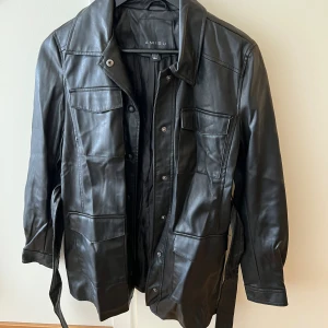 Skinn kappa - Medellång skinnkappa med knyte. Skrynklig pga att den har legad ihopvikt. Nyskick. Knappt använd. Går strax över rumpan 