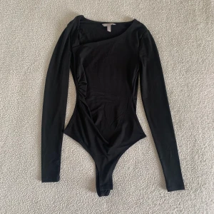 H&M svart asymmetrisk body - Snygg body från H&M med snedskuren hals. Använd endast en gång, i nyskick utan anmärkningar. Storlek XS men passar definitivt även en S då den är stretchig.