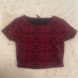 mörkröd mönstrad tröja - ganska kort mörkröd och svartmönstrad t-shirt köpt second hand och använd av mig ett fåtal gånger, otroligt fint skick men säljer då den inte kommer till användning
