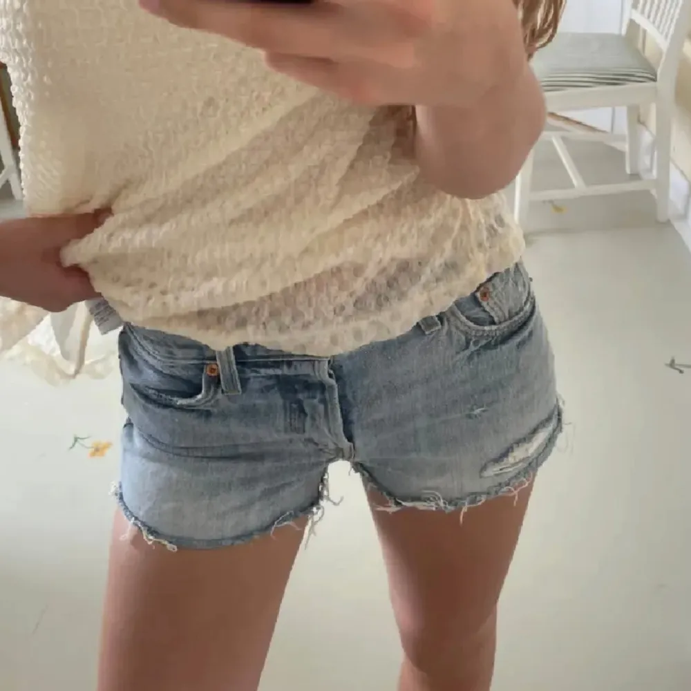 Använd gärna köp nu. Ett par blå jeansshorts från Levi's med slitna detaljer och råa kanter. Shortsen har en knappgylf och fem fickor.. Shorts.