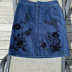 Blå jeanskjol - Blå jeanskjol med ett fint blommönster på! Köpt secondhand.