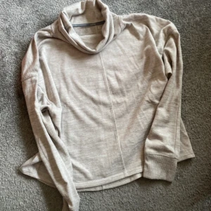 Beige polotröja från Calvin Klein - En beige polotröja från Calvin Klein med långa ärmar och ribbstickade muddar vid ärmslut och nederkant. Tröjan är tillverkad av polyester och spandex, vilket ger en bekväm och stretchig passform.