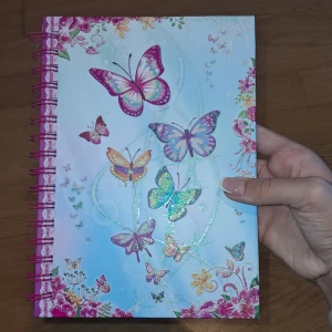 Jättefin fjärilsskrivbok  - Super fin skrivbok med fjärilar på. Ej linjerad och sidorna är i tre färger rosa,lila och blå. Vet inte vart den är ifrån fick den i present. Pris 30 kr