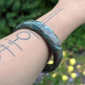 Natural Grön och brun marmorerad armband - Ett vackert armband med marmorerad design i gröna och bruna nyanser. Armbandet har en slät yta och en rund form, vilket gör det bekvämt att bära. Material ospecificerat, därför kategoriserat under 'Övrigt material  Vikten ca 26G  Mått står på bilder