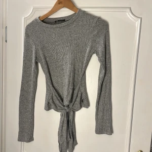 En stickad tröja med knut - Tröjan är i gott skick. Materialet är stickat. Knuten går att knyta om som man vill. Materialet är stretchigt 