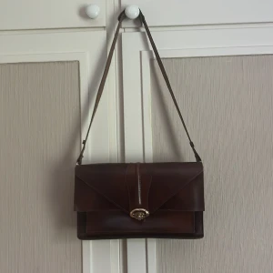 Liten brun vintage väska - Säljer denna jättesnygga bruna vintage väskan då det inte kommer till användning! I fint skick och bra material och köpt på en second hand. Finns 4 stora fack och öppnas genom att vrida på en liten guldig boll typ!