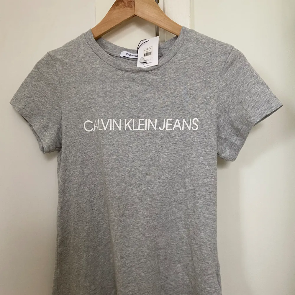 Säljer denna oanvända Calvin Klein T-shirt med lappen kvar. Nypris är 400 kr men den har dock en pytteliten fläck (se bild 2). Annars är den i nyskick. . T-shirts.
