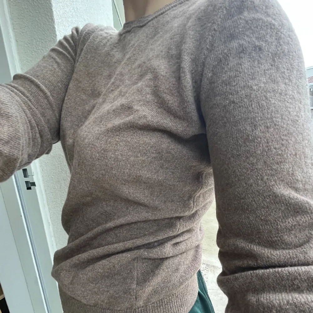 J. Lindeberg, stickad crewneck-tröja i storlek m. 70% super fine merino wool. 30% cashmere/kashmir. FĂ€rg mellan beige och brunt, lite melerad. Finns ett litet hĂ„l frampĂ„ som lĂ€tt gĂ„r lagas med nĂ„gra stygn, inga maskor har slĂ€ppt. Köpt secondhand âïž. Neuleet.
