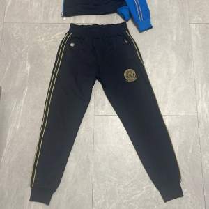 Säljer denna versace tracksuiten eftersom den inte längre passar mig. De är båda i bra skick. Byxorna är svarta och guldiga och koftan har en blandning av guld, svart, blå. Hör av dig vid fler bilder eller om du har frågor. 