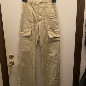 Cargo byxor  - Beige Cargo byxor i bra skick, ganska smala i midjan, bakfickorna är fejkar inte dem andra ,sidofikorna har knappar så att man kan stänga dem. Ser nya ut vet dock inte hur använda dem är i med att jag har fått från min kompis. 