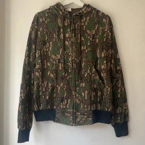 Vintage camo hoodie - Amerikansk vintage hoodie från Beyond Retro. Fint skogigt camo mönster, tyget är relativt tunt. Storleken är L, jag är XS för referens.