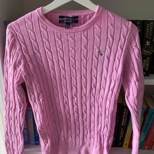 Rosa stickad tröja från GANT - Säljer en superfin rosa stickad tröja från GANT. Den är i storlek S och är gjord av stretchig bomull. Tröjan har ett snyggt kabelstickat mönster och är långärmad. Perfekt för höst och vinter! 💖