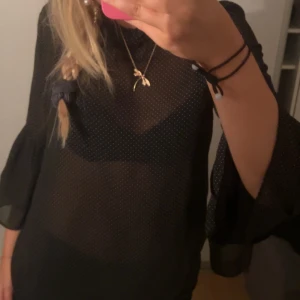 Svart klänning med trekvartsärm - Säljer en snygg svart blus  med trekvartsärm. Blusen är genomskinlig och har en lös passform, perfekt för fest eller en utekväll. Den är gjord av ett lätt och luftigt material som känns skönt mot huden. Blusen har en enkel men elegant design som gör den lätt att matcha med olika accessoarer.