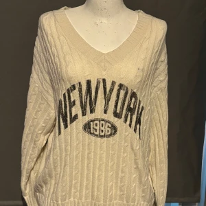 Vit stickad tröja från H&M Divided - Säljer en superfin vit stickad tröja från H&M Divided. Den har en snygg V-ringning och texten 'NEW YORK 1996' tryckt på framsidan. Tröjan är långärmad och perfekt för höst och vinter. Den är i storlek M och i bra skick. Perfekt för en casual look eller att mysa i hemma!