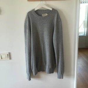 Grå stickad tröja från East West - Säljer en snygg och bekväm grå stickad tröja från East West. Tröjan är i storlek M och har en klassisk rund halsringning. Perfekt för höst- och vinterdagar när du vill hålla dig varm och stilren. Tröjan är i mycket bra skick och har ribbade muddar vid ärmslut och nederkant. Passar både till vardags och lite finare tillfällen. 🌟