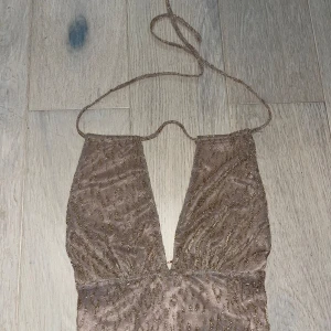Brun glittrig halterneck topp - Säljer en superfin brun glittrig halterneck topp. Den är croppad och har en djup v-ringning som ger en snygg och festlig look. Perfekt för en utekväll eller fest! Toppen är i bra skick och har en tight passform.