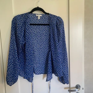 Blå prickig jacka - Säljer en superfin blå blus med vita prickar. Den är långärmad och har en normal passform. Den har en knytning framtill som ger en söt detalj. Perfekt för både vardag och fest!💙