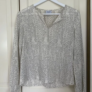 Vit blus med svarta prickar från Aware by Vero Moda - Säljer en superfin vit blus med svarta prickar från Aware by Vero Moda. Blusen har en v-ringad hals och långa ärmar med elastiska ärmslut. Perfekt för både vardag och fest! 🖤