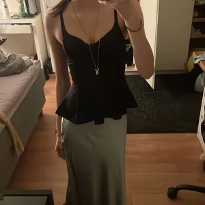 Svart topp från H&M Divided - Säljer en snygg svart topp från H&M. Toppen är ärmlös med smala axelband och har en peplum-design som ger en fin siluett. Perfekt för festliga tillfällen eller en utekväll. Toppen är i nyskick och redo att bäras av någon annan!🪩