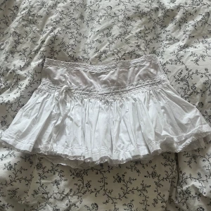 Vit minikjol - Jättesöt, vit minikjol från märket Papaya. Storlek 8 vilket motsvarar S. Söta spetsdetaljer och en liten rosett framtill, verkligen perfekt för sommaren!