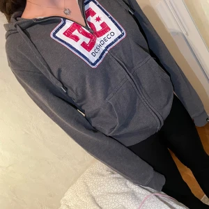 Grå zip-hoodie i märket DC shoes  - Tröjan är bra skick då den knappt är använd. Den är i storlek M, ganska sann till storlek men passar både M och S beroende på hur du vill att passformen ska vara😊