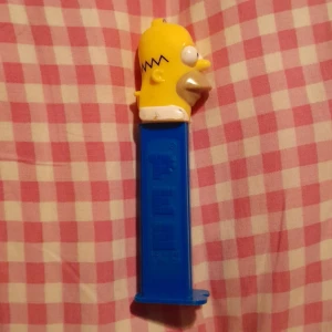 Homer Simpson PEZ dispenser - En PEZ dispenser med Homer Simpson från "The Simpsons". Lite färg har lossnat och man måste hålla i huvudet när man fyller på.