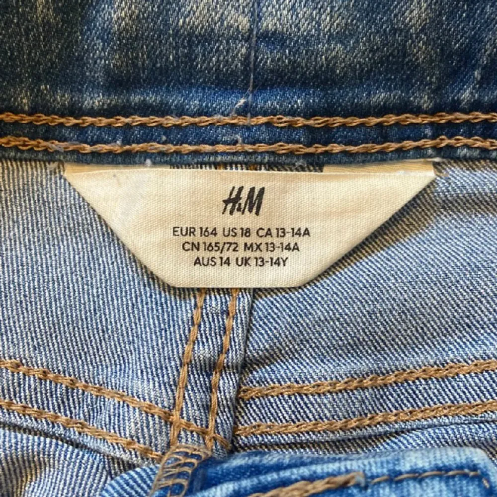 Säljer dess super snygga blå jeansshorts från H&M med slitna detaljer och spetsapplikationer på sidorna. Shortsen har en låg midja och fransiga kanter.. Shorts.