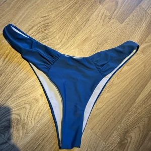 Blå bikiniunderdel - En blå bikiniunderdel. Underdelen har en enkel och stilren design med rynkade detaljer på sidorna. Endast provad utanpå byxor. Små i storlek. 