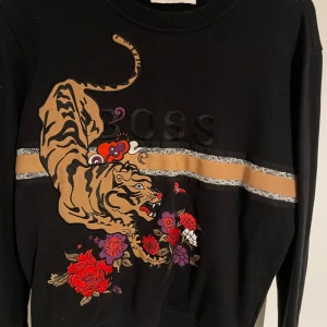 Svart tröja med tiger och blommor - En svart boss långärmad tröja med en stor tiger och blommor tryckta på framsidan. storlek s 