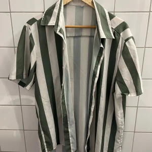 Grön randig kortärmad skjorta  - En grön kortärmad sommarskjorta i storlek L. Den är i använd skick och passar perfekt till sommaren