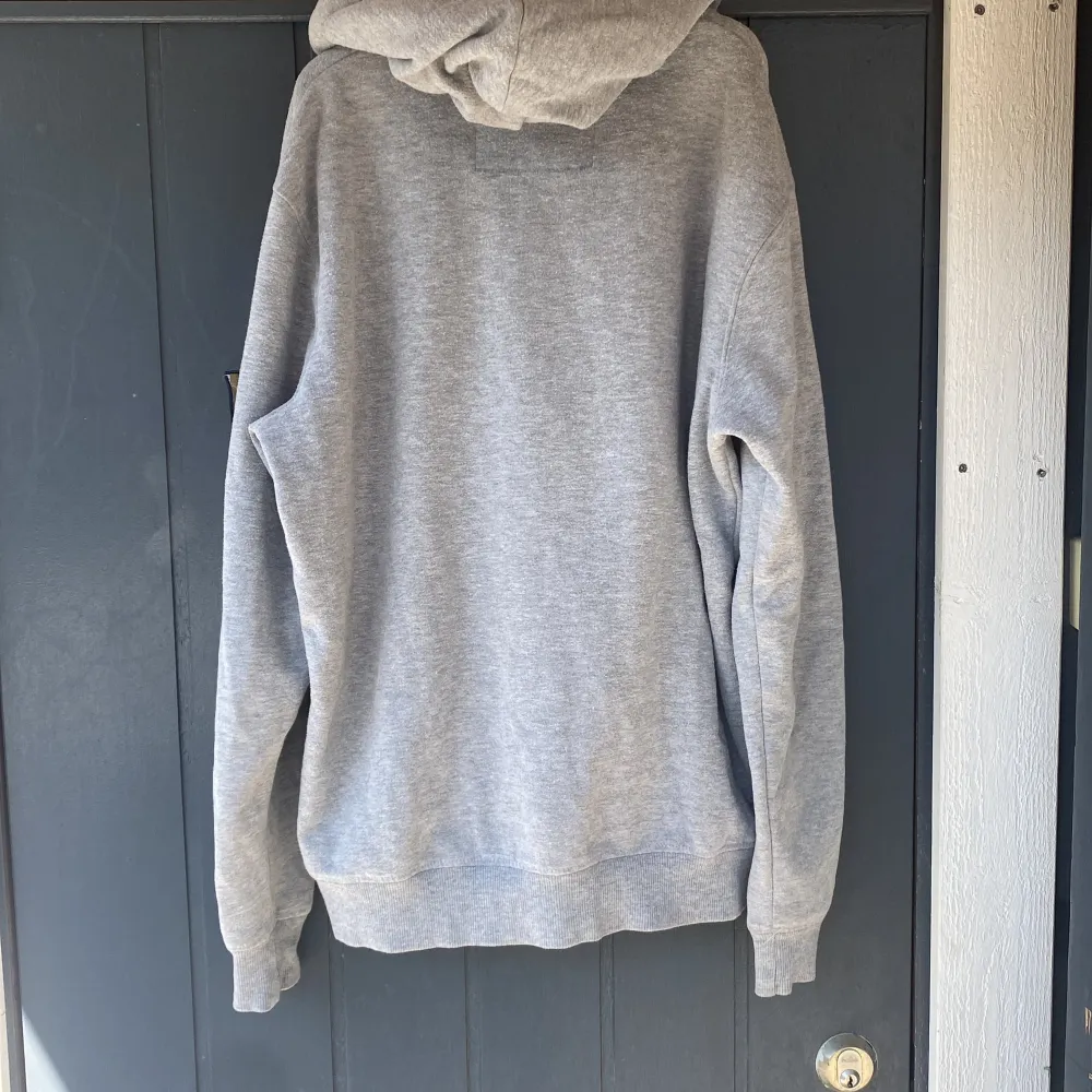 En bekväm grå hoodie från A.C.E med texten 'COLLECTIVE EVOLUTION' på framsidan. Hoodien har långa ärmar och ribbstickade muddar vid ärmslut och nederkant. Det finns även en detalj med texten 'A.C.E' på ärmen.. Tröjor & Koftor.