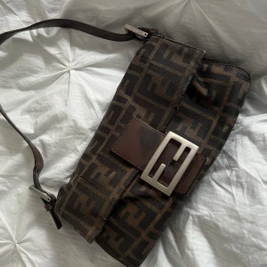 Fendi Zucca väska  - Väska från Fendi, köpt på luxurybyho och lagad då den vid köp hade en reva där bak, även sytt ihop handtaget på väskan när jag fick den. Fästet till låset har gått upp lite i tyget (se bild).   Fråga bara om fler bilder vid seriöst intresse!