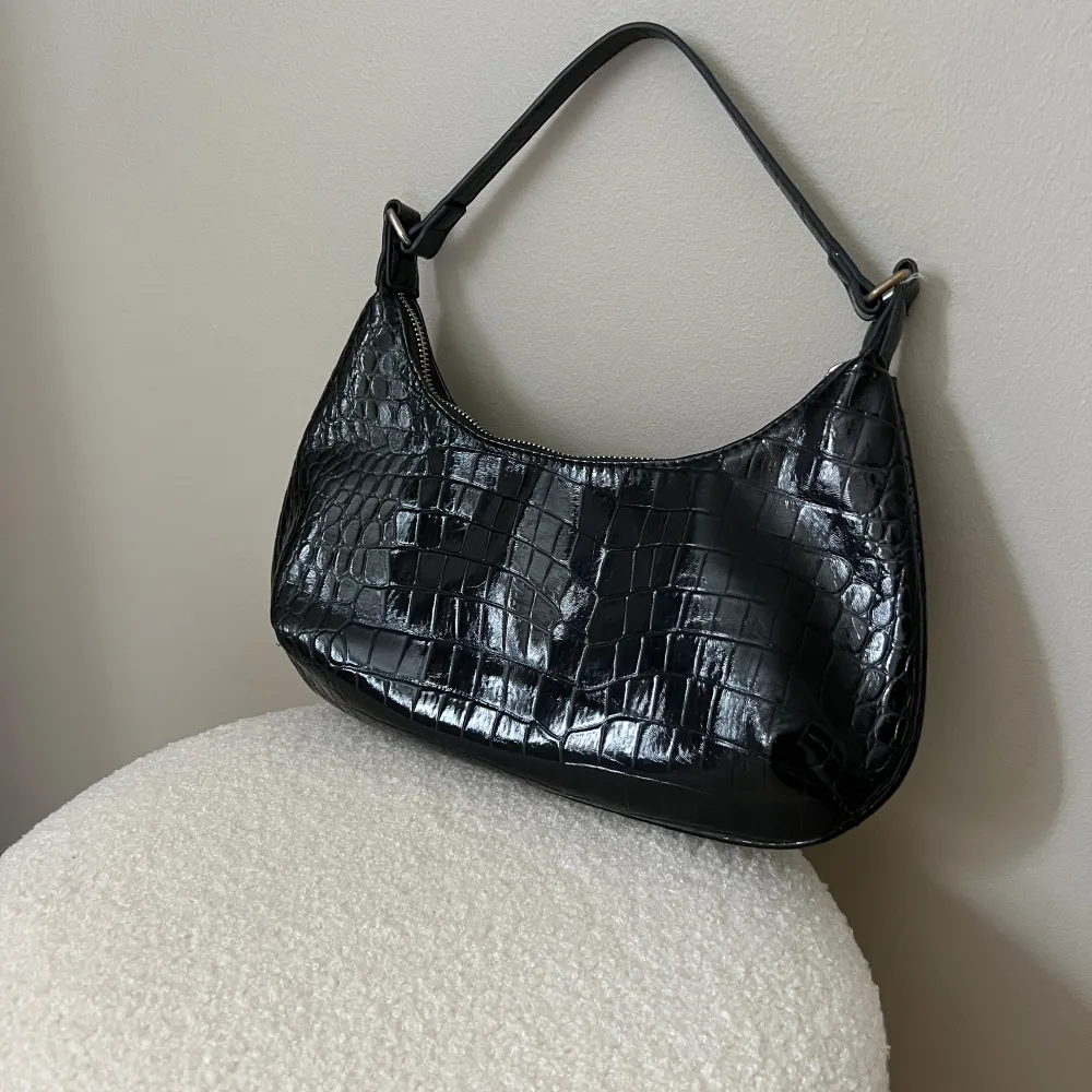 En svart handväska från Gina tricot med glansigt material. Materialet är ”Krokodilskinn” . Laukut & Käsilaukut.