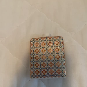 Parfymflaska med mönster - En parfymflaska med ett detaljerat mönster i blått, orange och guld. Flaskan har en fyrkantig form och en genomskinlig kork.