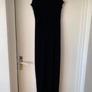 Svart långklänning med pärldetaljer - En elegant svart långklänning med pärldetaljer runt halsringningen och ärmhålen. Klänningen är ärmlös och har en tight passform som framhäver figuren.