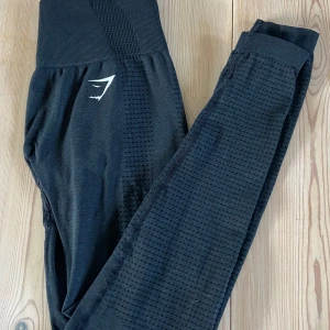 Gymshark träningstights - Ett par mycket fina träningstights från Gymshark som bara är använda ett fåtal gånger då dom är för små💗Dom är mycket sköna och sitter jättebra i midjan! Ljuset får dom att se gråa ut men dom är svarta/mörkgråa med lite detaljer.