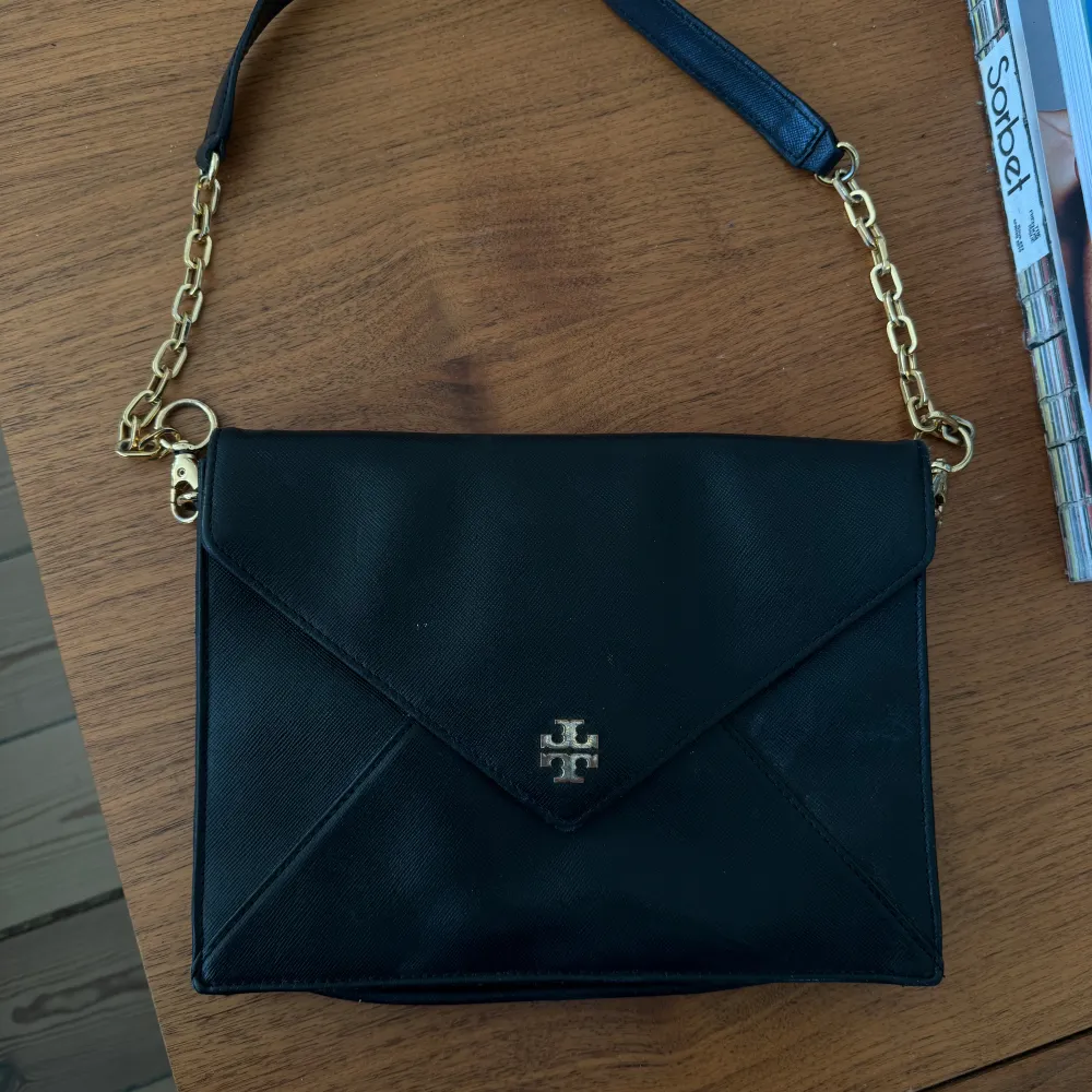 Tory burch clutch i svart med guldetaljer. Lädret är i fint skick men tyvärr är detaljerna lite slitna. . Accessoarer.